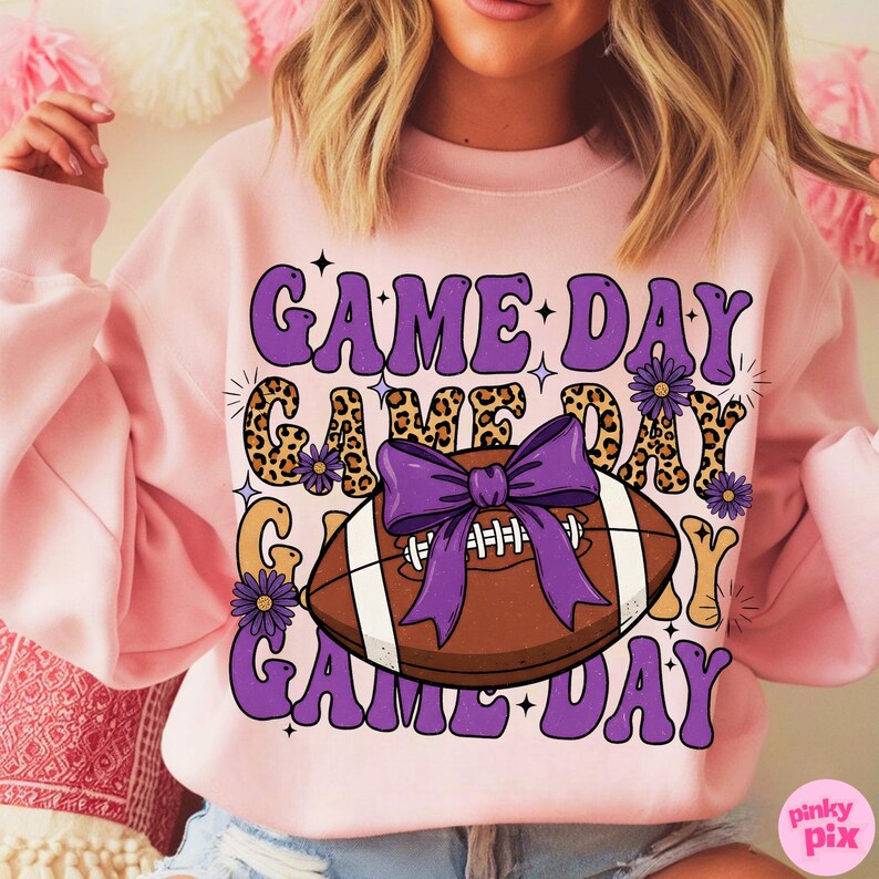 May include: Pink sweatshirt with the words "GAME DAY" in purple, with a football graphic. The football is brown with white stripes and a purple bow. The words "GAME DAY" are also in a leopard print.