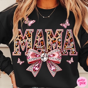 May include: Black sweatshirt with the word "MAMA" in leopard print, outlined in pink rhinestones. A large pink bow with a crystal center and rhinestones is below the word. Pink butterflies are scattered around the design.