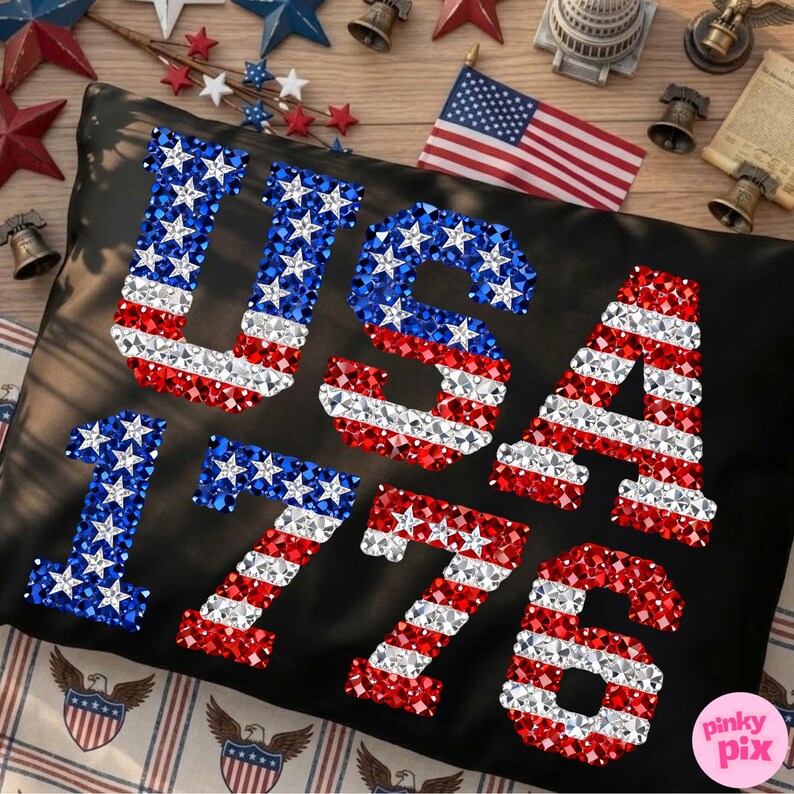 K&ouml;nnte beinhalten: Schwarzes Kissen mit dem Wort "USA" und der Zahl "1776" in rot, wei&szlig; und blau glitzernden Verzierungen, die an die amerikanische Flagge erinnern. Das Bild enth&auml;lt dekorative Glocken und Sterne.