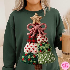 May include: A dark green sweatshirt featuring a detailed, handcrafted Christmas tree design. The tree is composed of various textured sections, including red plaid, white hearts, and green holly patterns, topped with a star and a pink bow. The overall aesthetic is festive and handmade.
