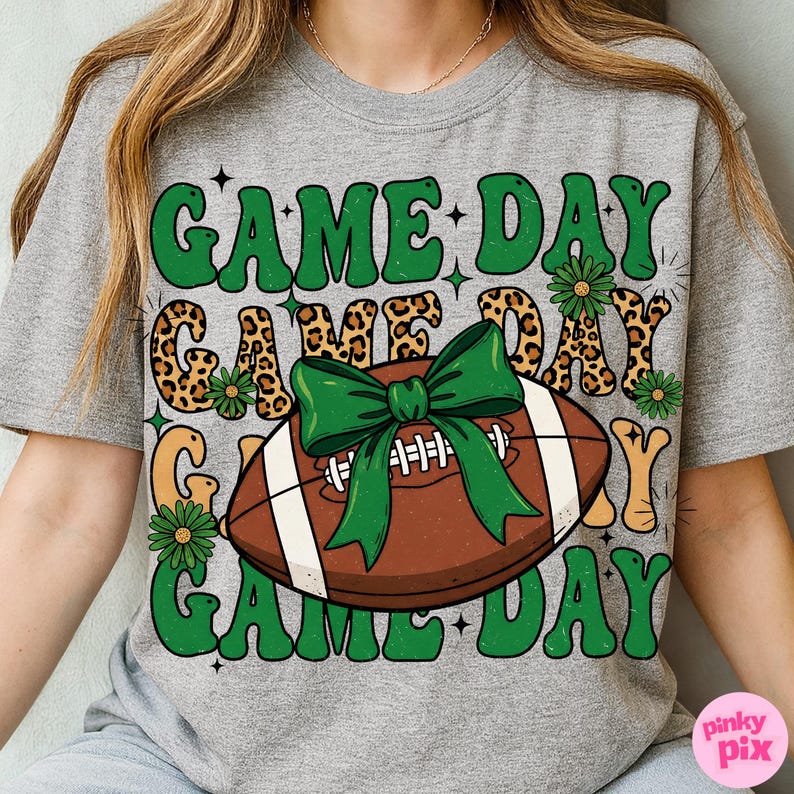 May include: Gray t-shirt with a football graphic and the words "GAME DAY" in green, with a leopard print design. The football has a green bow. The shirt is a casual, sporty style.