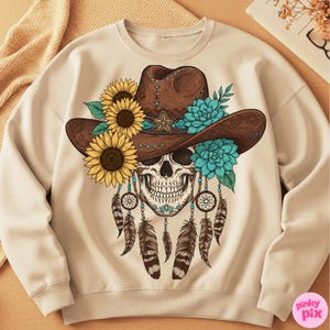 Op de afbeelding: Cr&egrave;mekleurige sweatshirt met een schedel die een bruine cowboyhoed draagt, versierd met zonnebloemen en turquoise bloemen. De schedel heeft dromenvangers en veren. Een uniek en artistiek ontwerp.