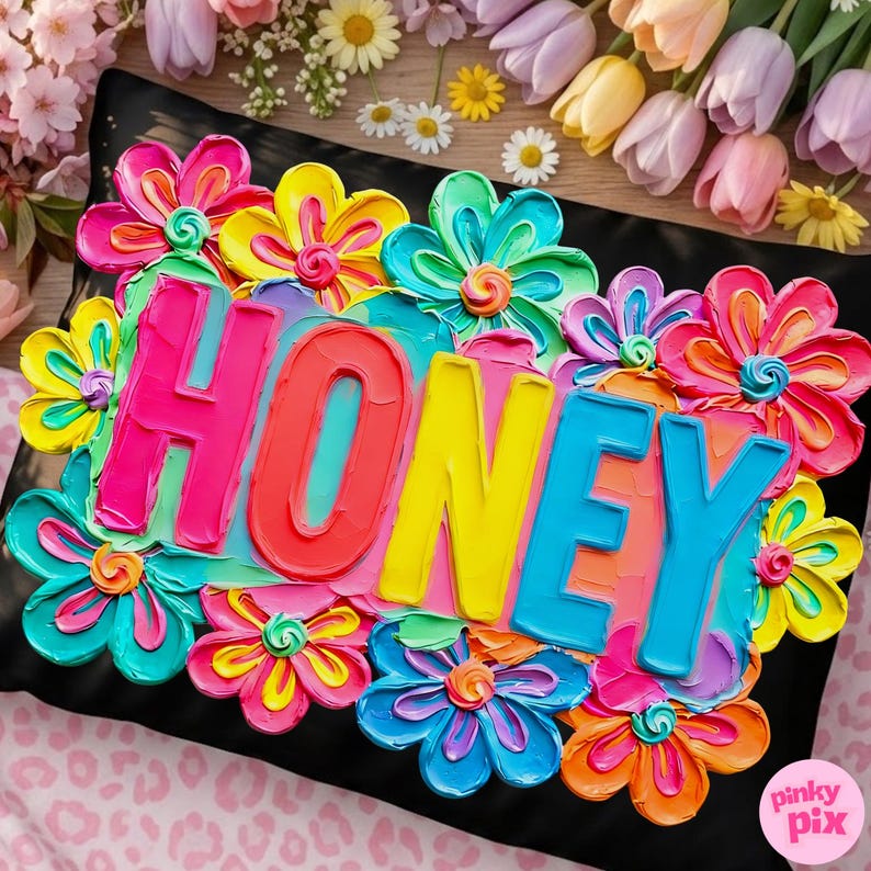 May include: A black pillow decorated with colorful, textured flowers and the word "HONEY" in bright, bold letters. The flowers are in shades of pink, yellow, blue, and orange, creating a vibrant and cheerful design.