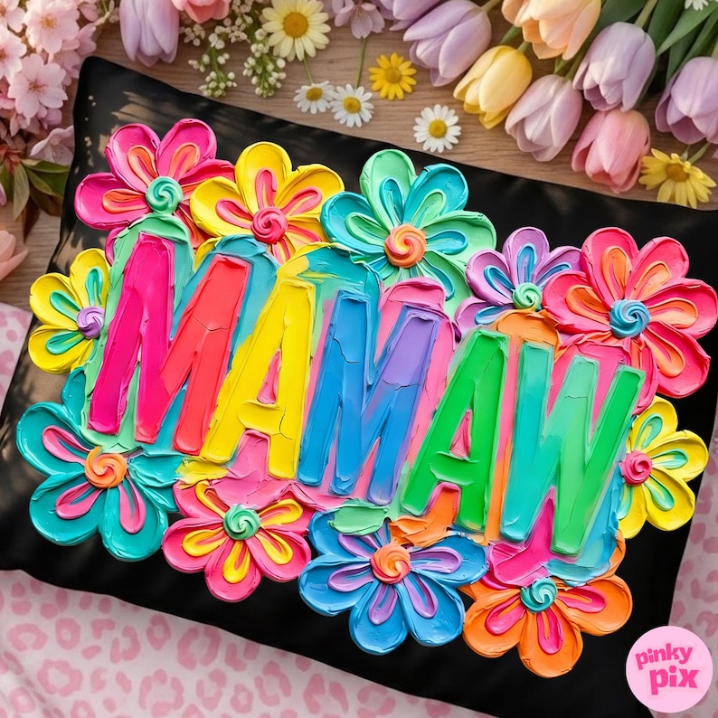 May include: Black decorative pillow with the word "MAMAW" in bright, textured letters, surrounded by colorful, textured flowers in shades of pink, yellow, blue, and orange. The pillow is a square shape.