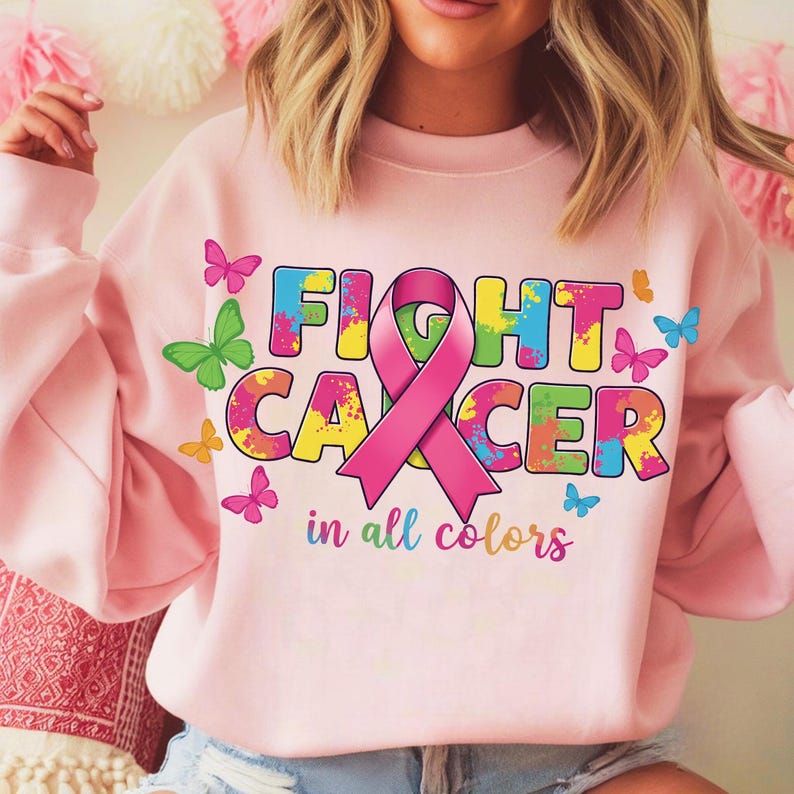 May include: Pink sweatshirt with the words "FIGHT CANCER" in colorful letters and a pink ribbon. The design includes butterflies in various colors. The phrase "in all colors" is printed below the main text.