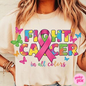 May include: Cream-colored t-shirt with the words "FIGHT CANCER" in colorful, splattered letters, a pink ribbon, and the phrase "in all colors." Butterflies in various colors surround the text. The shirt is a casual style.