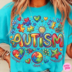May include: A turquoise t-shirt with a colorful graphic design. The design includes the word "AUTISM" in rainbow colors, puzzle pieces, hearts, flowers, and the words "accept", "love", and "understand".