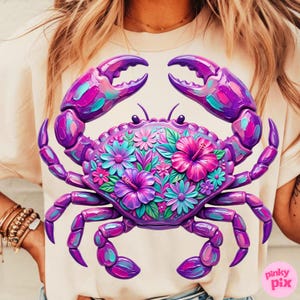 May include: A light beige t-shirt featuring a vibrant, stylized crab design. The crab is rendered in shades of purple, pink, and teal, with intricate floral details filling its body. The design includes the text "pinky pix" in the lower right corner.