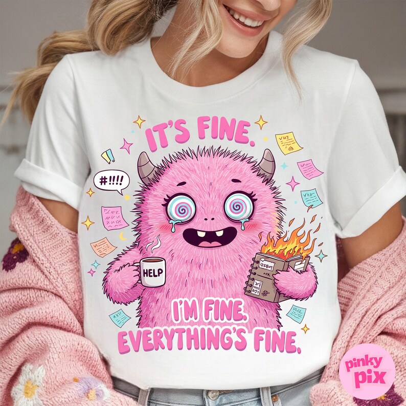 May include: White t-shirt with a pink monster graphic. The monster has a big smile, is holding a cup of coffee that says "Help" and a notebook with flames coming out of it. The text on the shirt says "It's fine. I'm fine. Everything's fine."