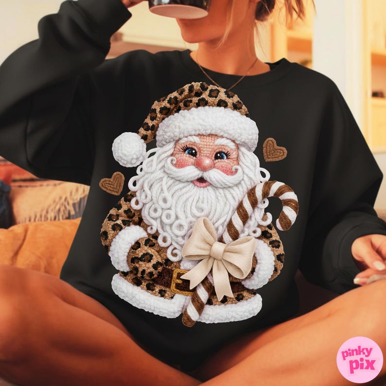 May include: Black sweatshirt featuring a Santa Claus design with a leopard print hat and coat trim. The Santa Claus has a white beard and holds a candy cane. A cream-colored bow is at the bottom of the Santa Claus design.