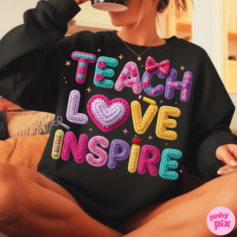 Pu&ograve; includere: Felpa nera con le parole "TEACH LOVE INSPIRE" in lettere colorate e strutturate. Il design include un cuore, forbici, una matita e un fiocco. La felpa &egrave; uno stile girocollo.