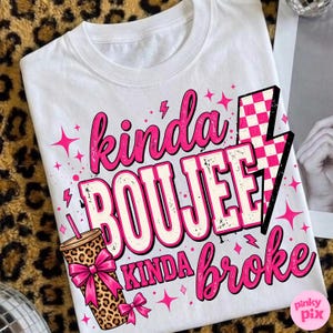 May include: A white t-shirt featuring the text "kinda BOUJEE kinda broke" in pink and white lettering. The design includes a leopard print tumbler with a pink bow, a pink and white checkered lightning bolt, and small pink star accents.