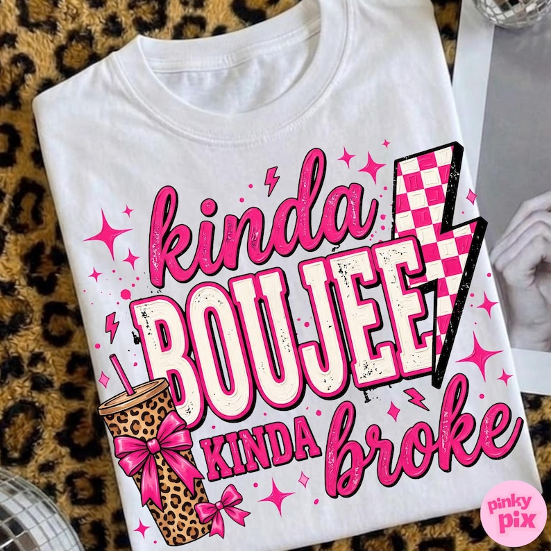 May include: A white t-shirt featuring the text "kinda BOUJEE kinda broke" in pink and white lettering. The design includes a leopard print tumbler with a pink bow, a pink and white checkered lightning bolt, and small pink star accents.