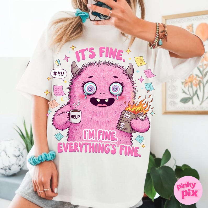 May include: White t-shirt with a pink monster illustration. The monster is holding a cup that says "Help" and a notebook with flames coming out of it. The text on the shirt says "It's fine. I'm fine. Everything's fine."
