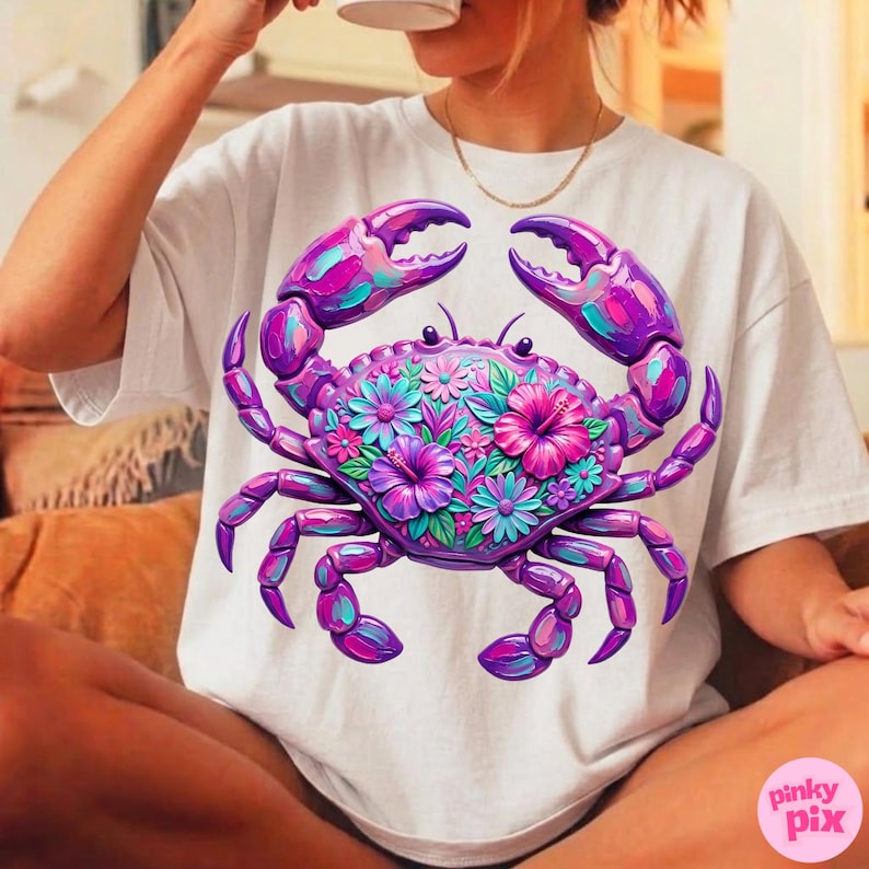 May include: White t-shirt featuring a vibrant, floral crab design. The crab is depicted in shades of purple, pink, and teal, with intricate floral details on its shell. The design is centered on the shirt, creating a bold and eye-catching graphic.