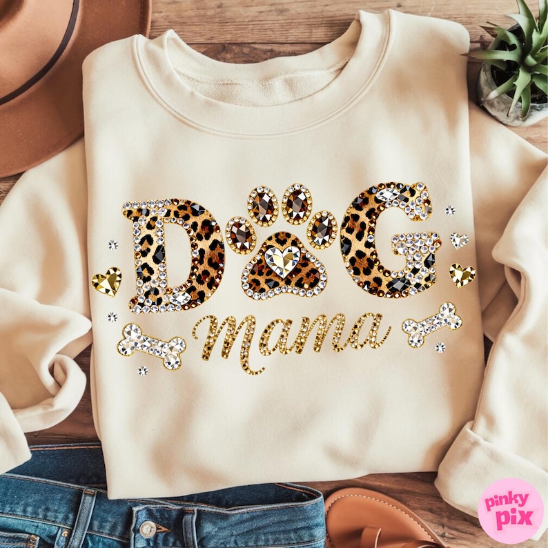 May include: Cream-colored sweatshirt with the text "DOG Mama" in a mix of leopard print and rhinestone embellishments. The design includes a paw print with a heart and bone accents, perfect for dog lovers.