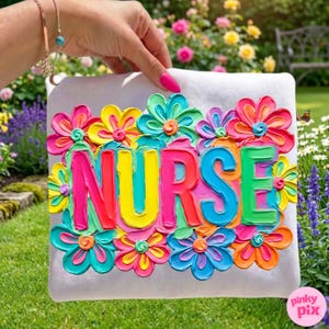 May include: A white square pillow with the word "NURSE" in vibrant, raised lettering, surrounded by colorful, textured flowers. The flowers feature shades of pink, yellow, blue, and orange. The pillow is held against a backdrop of green grass and flowers.