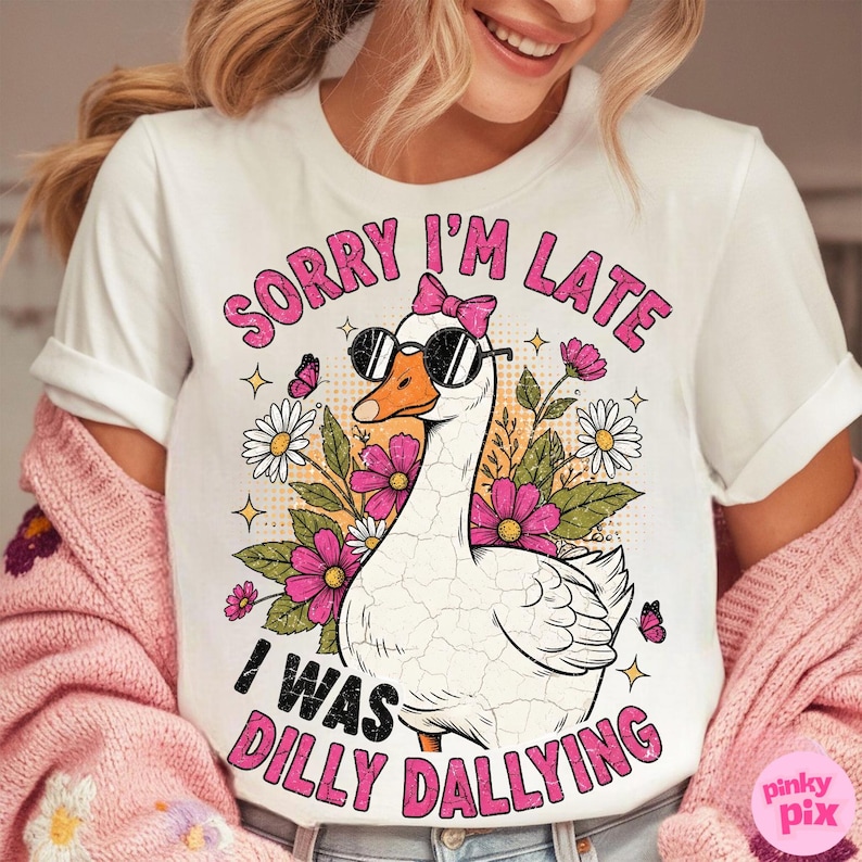 K&ouml;nnte beinhalten: Wei&szlig;es T-Shirt mit einer Grafik einer Gans mit Sonnenbrille und rosa Schleife. Der Text lautet "Sorry I'm Late, I Was Dilly Dallying" in Pink. Das Design umfasst Blumen und Schmetterlinge.