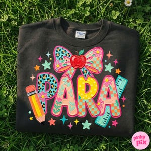 May include: Dark gray sweatshirt with a colorful "PARA" design. The design includes a bow with an apple, a pencil, a ruler, and stars. The letters are decorated with floral and leopard print patterns.