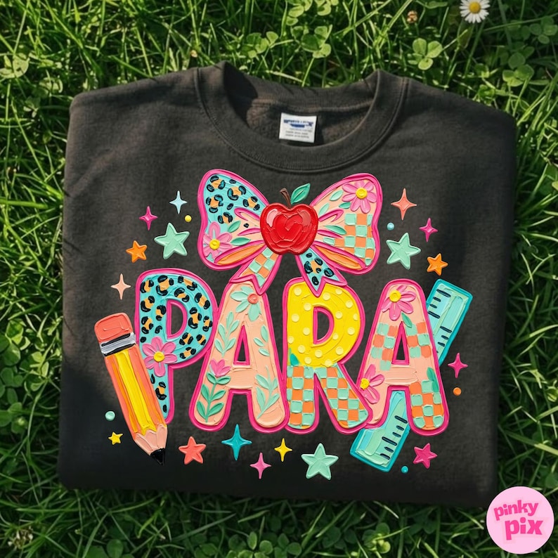 May include: Dark gray sweatshirt with a colorful "PARA" design. The design includes a bow with an apple, a pencil, a ruler, and stars. The letters are decorated with floral and leopard print patterns.