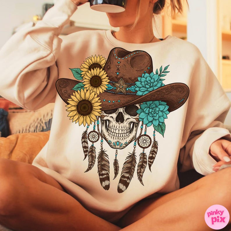 Op de afbeelding: Beige sweatshirt met een schedel die een bruine cowboyhoed draagt, versierd met zonnebloemen en turquoise bloemen. De schedel heeft dromenvangers en veren. Het ontwerp is een mix van Western- en Boheemse stijlen.