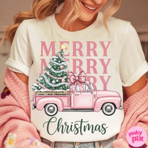 May include: White t-shirt with a pink Christmas design. The design features a pink truck carrying a Christmas tree and a large bow. The words "MERRY MERRY CHRISTMAS" are printed above and below the truck.