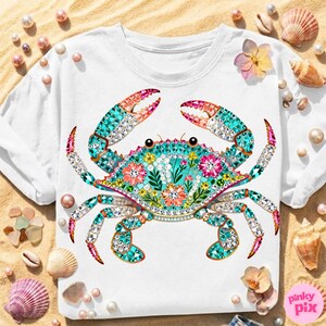 May include: White t-shirt featuring a detailed, jewel-toned crab design. The crab is adorned with turquoise, pink, and clear crystals, with floral accents. The design includes the text "pinky pix" in the lower right corner.