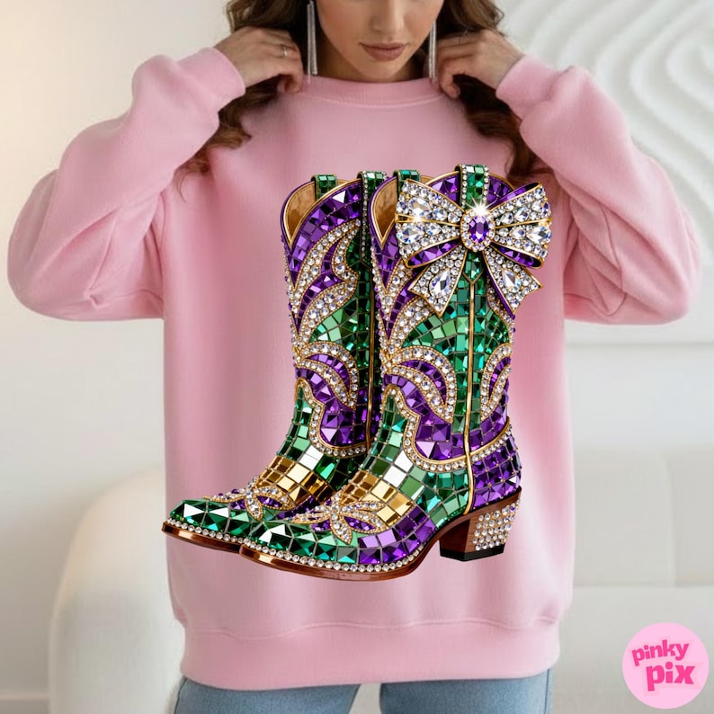 May include: Pink sweatshirt featuring a vibrant graphic of jeweled cowboy boots. The boots are adorned with green, purple, and gold mosaic-style embellishments, and a large bow with sparkling details. The boots have a brown heel and are set against a white background.