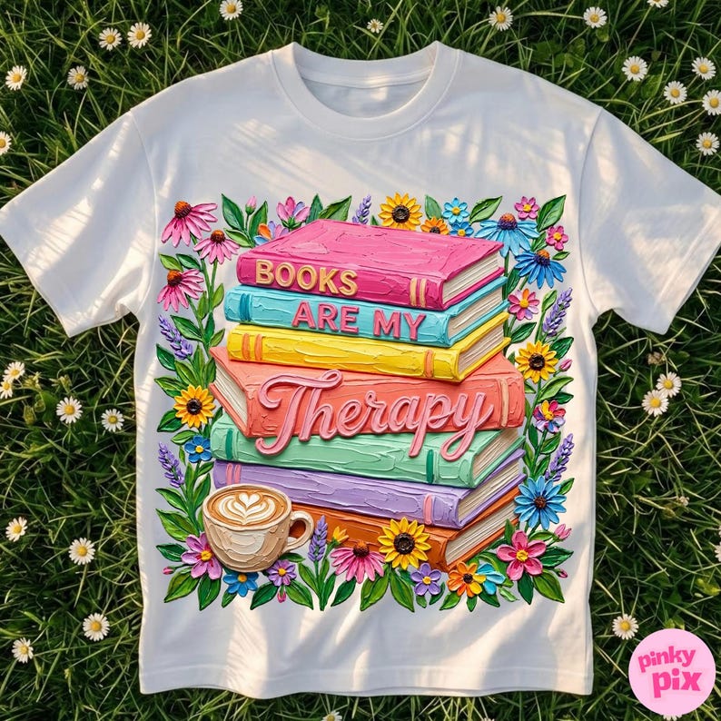May include: White t-shirt featuring a colorful design of stacked books with the text "BOOKS ARE MY THERAPY." The design includes a coffee cup and floral accents in pink, blue, yellow, and orange.