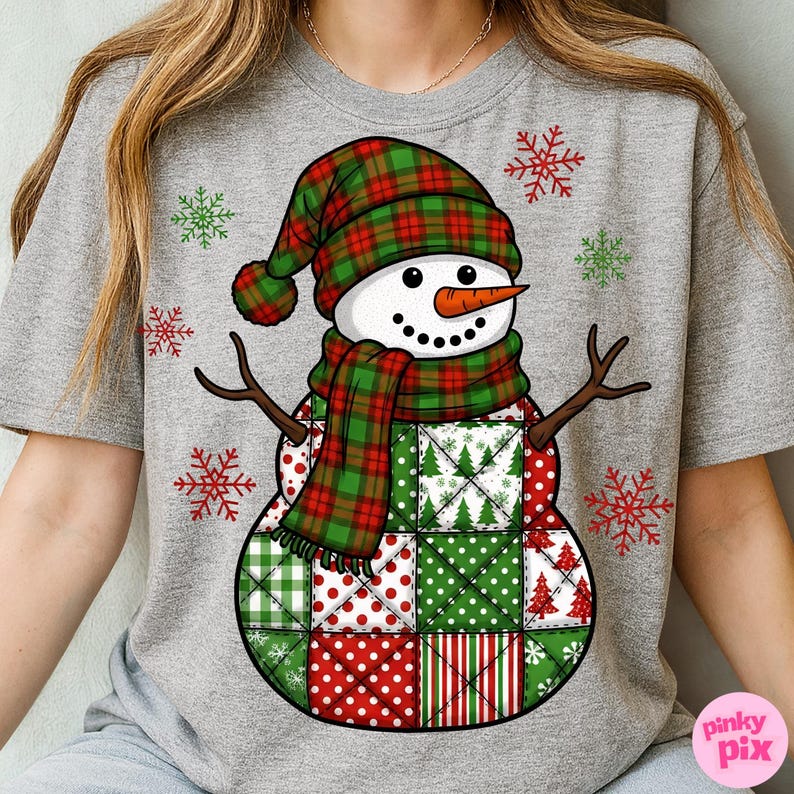 May include: A gray t-shirt featuring a snowman design. The snowman has a plaid hat and scarf in red and green, a carrot nose, and twig arms. The snowman's body is made of patchwork squares in red and green patterns. Red and green snowflakes are scattered around the design.