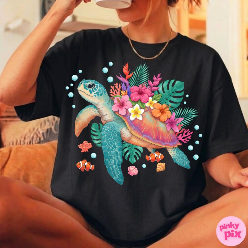 May include: Black t-shirt featuring a colorful sea turtle design. The turtle has a blue shell and is surrounded by tropical flowers, leaves, and fish. The design includes pink, orange, and yellow flowers, and the text "pinky pix" is in the bottom right corner.