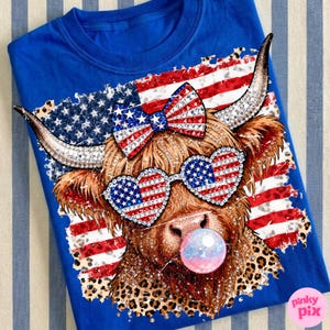 May include: Royal blue t-shirt featuring a whimsical cow design. The cow wears heart-shaped sunglasses and a bow, both adorned with an American flag pattern. The design includes a bubble and a leopard print.