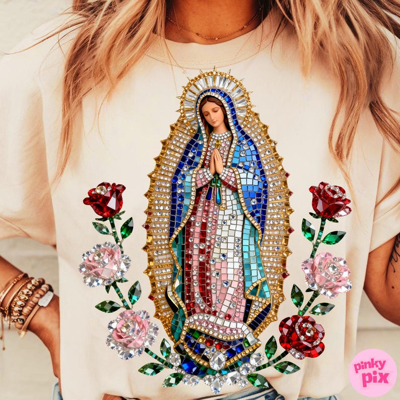 May include: Cream-colored t-shirt featuring a mosaic-style image of the Virgin Mary, adorned with sparkling embellishments. The design includes a halo, blue and red robes, and is flanked by jeweled roses. The text "pinky pix" is visible.