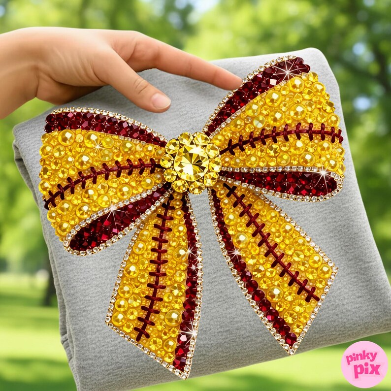 May include: A large, decorative bow with a softball design. The bow is embellished with yellow and burgundy rhinestones, and a central yellow jewel. Red stitching details add to the sparkling, eye-catching accessory.