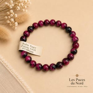 Op de afbeelding: Een ronde kralenarmband gemaakt van gepolijste Robijn in Zoisiet stenen met diep magenta en zwarte gevlekte patronen. Een klein rechthoekig label aan de armband toont de tekst Rubis Trace Zoïsite AAA 07-08mm.
