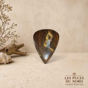 Peut inclure: Un plat en pierre en forme de goutte d'eau présentant une surface polie brun foncé avec des motifs tourbillonnants d'inclusions minérales dorées et bleu clair. L'objet a une finition lisse et brillante avec une base pointue et des variations naturelles.