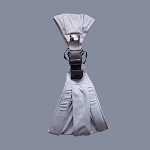 Könnte beinhalten: Eine graue Babytrage mit schwarzer Schnalle und Riemen. Die Trage hat ein strukturiertes Design mit Kopfstütze und einer Tasche. Der Text "Best Ever" ist auf der Trage sichtbar.