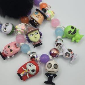 May include: A colorful beaded accessory featuring character charms from "The Nightmare Before Christmas." The charms include Jack Skellington, Sally, and other characters. The beads are in various colors, including pink, blue, and purple. A black fuzzy charm is at the top.