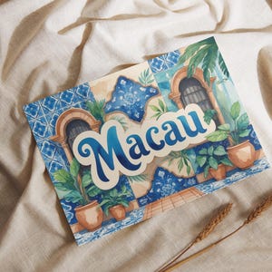 Puede incluir: Ilustración en acuarela de Macao con el nombre de la ciudad en una fuente estilizada. La obra presenta patrones de azulejos azules y blancos, ventanas arqueadas, plantas en macetas y una paleta de colores cálidos.