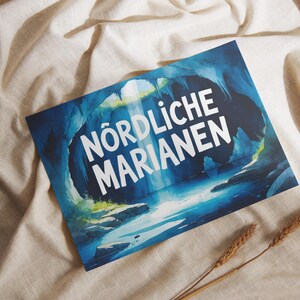Könnte beinhalten: Ein rechteckiger Druck mit den weißen Worten "NORDLICHE MARIANEN" vor einer blau-türkisfarbenen Unterwasserszene. Der Druck liegt auf einem beigen Stoff, mit zwei Weizenähren im Vordergrund.