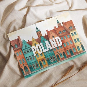 Puede incluir: Ilustración en acuarela de edificios coloridos con la palabra "POLAND" en blanco. Los edificios tienen fachadas rojas, turquesas, amarillas y naranjas. La imagen está sobre un fondo de tela beige con espigas de trigo.