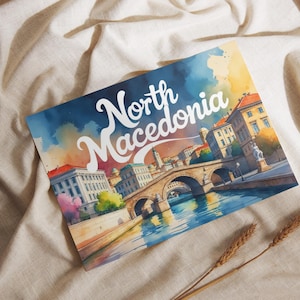 Könnte beinhalten: Aquarelldruck von Nordmazedonien mit einer Brücke über einem Fluss und Gebäuden. Der Text "North Macedonia" ist in weißer Schrift gehalten. Der Druck hat einen farbenfrohen, künstlerischen Stil mit blauen, gelben und orangenen Farbtönen.