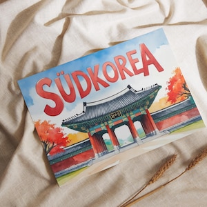 Puede incluir: Impresión en acuarela de un monumento de Corea del Sur con la palabra "SÜDKOREA" en rojo. La imagen presenta una puerta tradicional coreana con columnas rojas, un tejado negro y árboles de otoño. La impresión está sobre una tela beige.