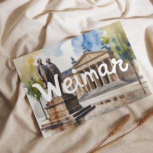 May include: Watercolor print of Weimar, Germany, featuring a building with columns and statues of two men. The word "Weimar" is written in white script. The print is on a beige surface with two stalks of wheat.