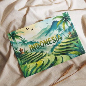 Op de afbeelding: Een aquarel illustratie van Indonesië met rijstterrassen, palmbomen en bergen. Het woord "INDONESIA" is in groene letters geschreven. Het kunstwerk staat tegen een beige stoffen achtergrond.