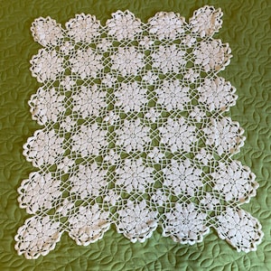 May include: A rectangular white crochet doily featuring a repeating pattern of interconnected floral motifs. The design consists of multiple circular flower shapes joined by a delicate lattice of thread, creating a scalloped edge along the perimeter.