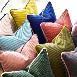 Op de afbeelding: Een verzameling decoratieve kussens in verschillende kleuren en texturen. De kussens zijn gemaakt van corduroy stof en hebben een pompon rand.