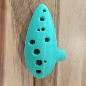 May include: A turquoise ocarina with eight finger holes. The ocarina is a wind instrument that is often used in fantasy and video games.
