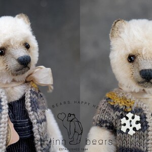 May include: A plush bear with cream-colored fur, dark eyes, and a black nose. It wears a knitted vest in shades of gray and mustard yellow, featuring a white snowflake-shaped button and a light beige ribbon tied around its neck.