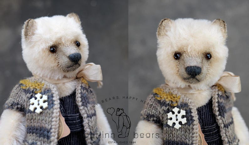 May include: A plush bear with cream-colored fur, dark eyes, and a black nose. It wears a knitted vest in shades of gray and mustard yellow, featuring a white snowflake-shaped button and a light beige ribbon tied around its neck.